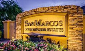 Un panneau indiquant l’entrée du lotissement SamMarcos Country Club Estates, avec une arche en pierre et un parterre de fleurs devant.