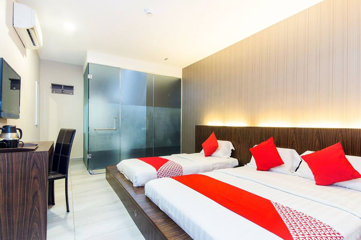 A hotel room with two beds, a desk, a chair, and a shower area.