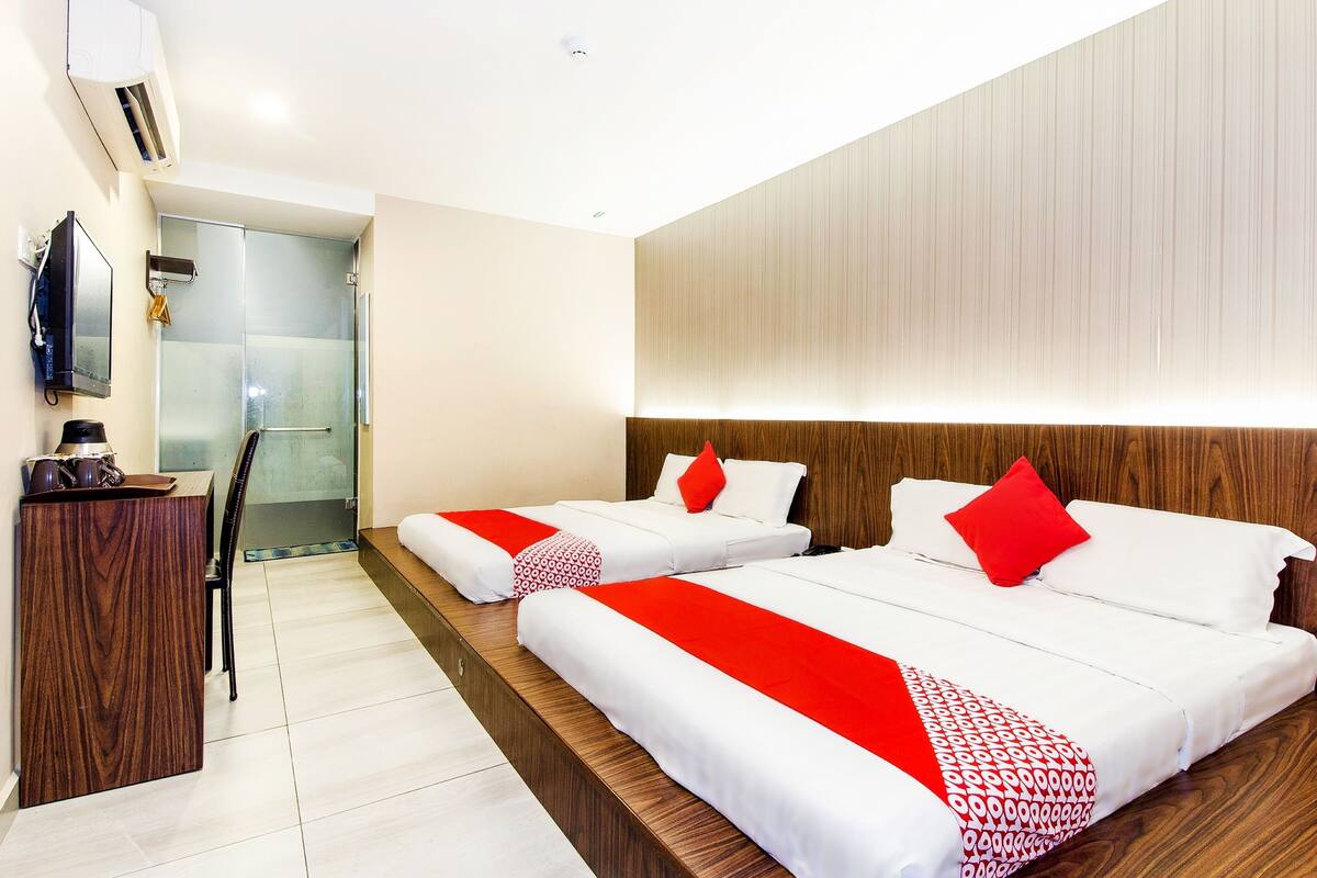 A hotel room with two beds, a desk, and a shower area.