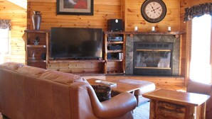 Un interior de madera con un sofá de cuero, un televisor de pantalla plana, una chimenea y un reloj en la pared.