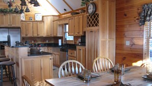 Interior de una cabaña de madera con cocina, comedor y asientos tipo barra.
