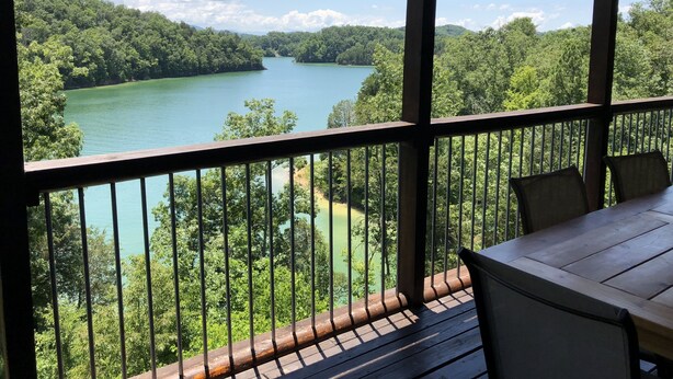 Terraza de madera con mesa y sillas con vista a un río rodeado de un bosque denso.