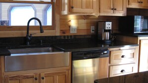 Una cocina con armarios de madera, un lavamanos de acero inoxidable, lavavajillas, cafetera y microondas.