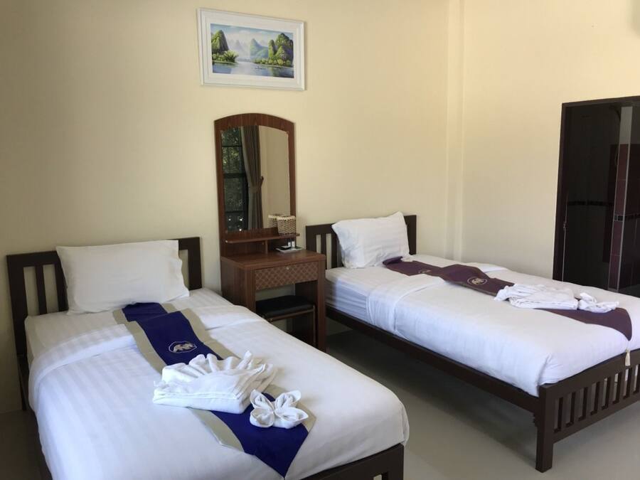 Two single beds with white linens, a wooden nightstand, a mirror, and a framed picture on the wall.