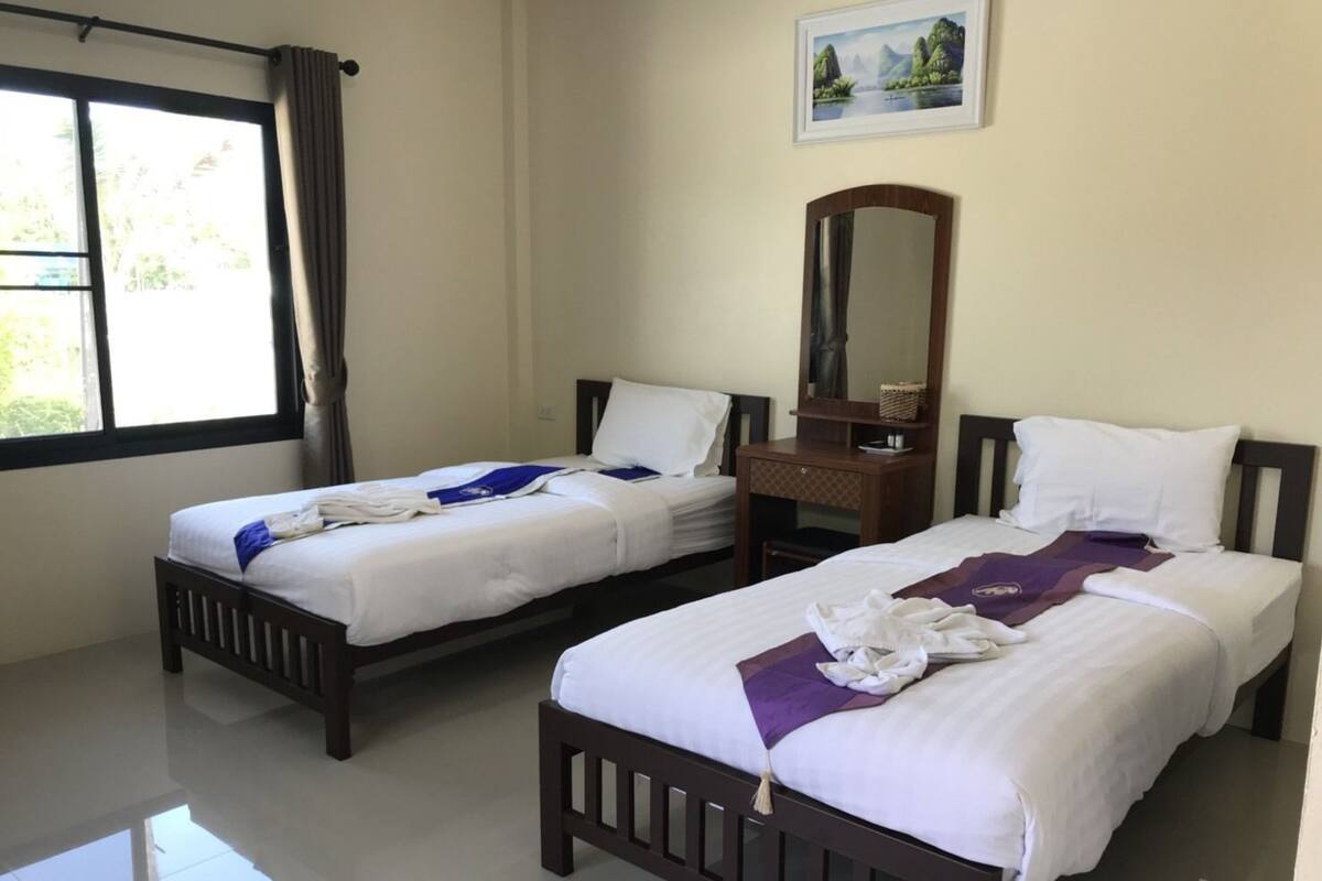 A hotel room with two beds, a wooden dresser, a mirror, and a window with curtains.