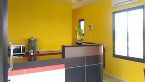 Une cuisine avec des murs jaunes, un four à micro-ondes, une machine à café et une fenêtre avec des stores.