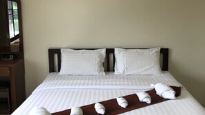 Un lit bien fait, avec du linge de lit blanc et un plaid marron, un tableau encadré au mur et une table de chevet en bois avec une lampe.