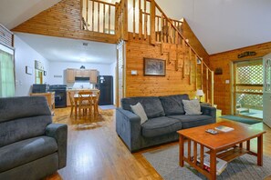 A spacious living area with a wooden staircase, a gray sofa, a wooden coffee table, and a kitchen in the background.