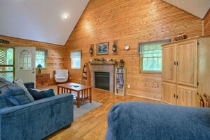 A cozy living room with wooden walls, a fireplace, a sofa, a coffee table, and a bookshelf.