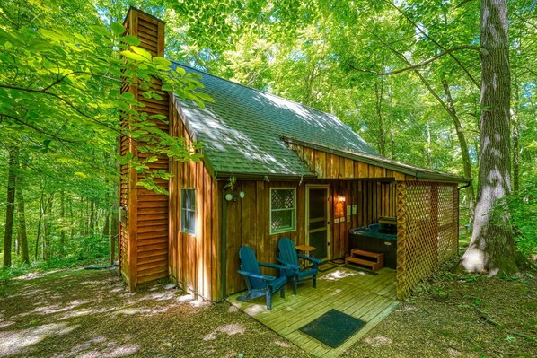 A cabin with a wooden exterior, a porch with two chairs, and a small deck. - The Loft at Hiding Place Cabins (Logan)