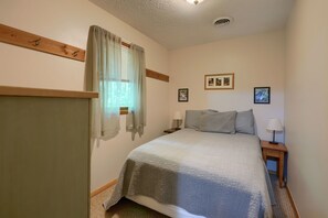 Un dormitorio con cama, dos mesitas de noche, una ventana con cortinas e imágenes colgadas en la pared.