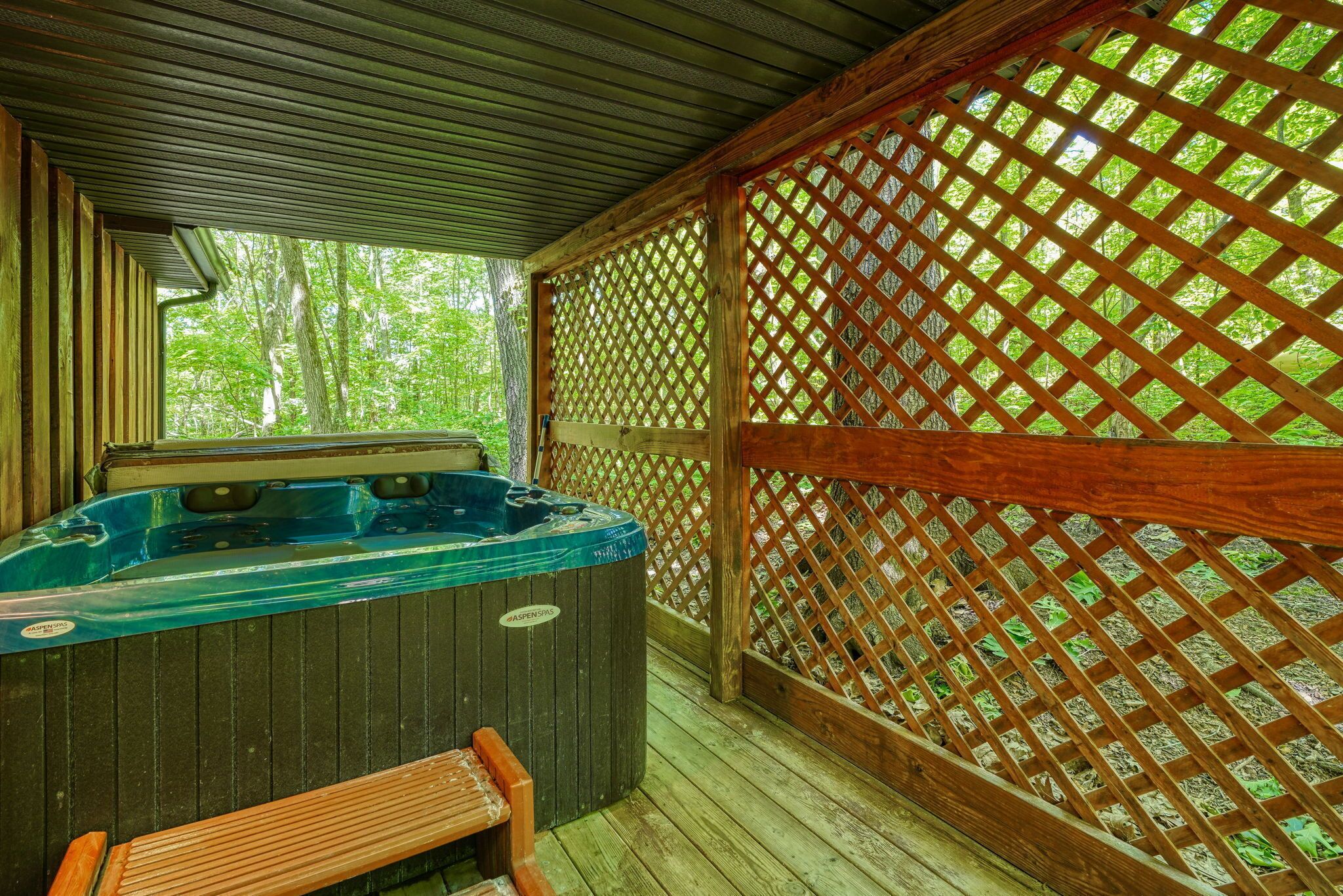 A hot tub area with a wooden deck, a wooden fence, and a view of trees.