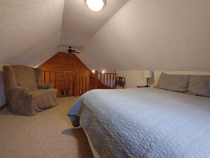 Um quarto com uma cama grande, uma cadeira, um abajur e um ventilador de teto.