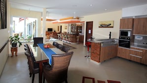 Una cocina moderna con una isla central, un comedor con una mesa azul y una barra con taburetes.