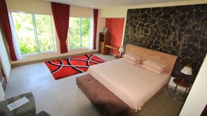 Un dormitorio con una cama grande, una pared decorada con piedra, un tapete rojo y vistas a la vegetación por la ventana.
