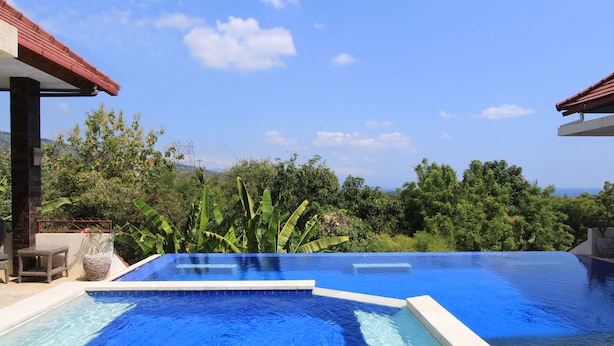 Una piscina infinita con una característica de agua azul cristalina, rodeada de exuberante vegetación y vistas a colinas distantes.
