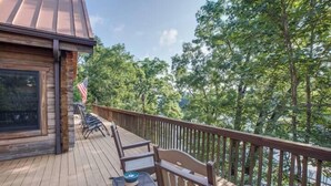 A wooden deck with outdoor seating, a flag, and a view of trees. - Ten Mile Cabin Sleeps 16! Best Deal on AirBNB (Ten Mile)
