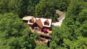 A cabin surrounded by dense forest, with a prominent chimney and a pink umbrella visible. - Ten Mile Cabin Sleeps 16! Best Deal on AirBNB (Ten Mile)