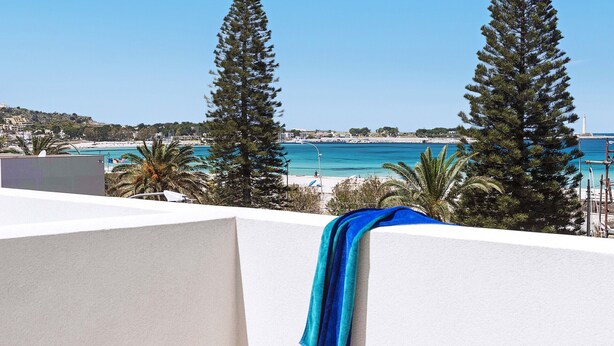 Un balcon avec vue sur une plage, de grands arbres et un ciel bleu dégagé.