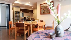 Un'area pranzo con un tavolo e sedie in legno, un vaso con fiori e una cucina sullo sfondo.