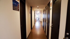 Un corridoio d'albergo con porte su entrambi i lati, un pavimento in legno e un poster sulla parete sinistra.
