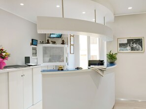Un espace d’accueil doté d’un comptoir blanc incurvé, d’un téléviseur fixé au mur et d’une photographie encadrée placée au-dessus du comptoir.
