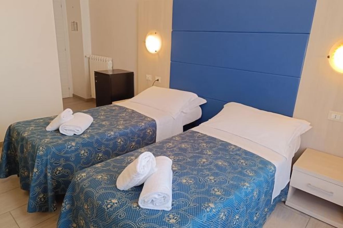 Een kamer met twee bedden, elk voorzien van een bedspreide met dessin en witte kussens, en een nachtkastje ertussen.