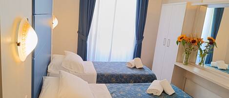 A hotel room with two beds, a large mirror, a TV, and a window with curtains.