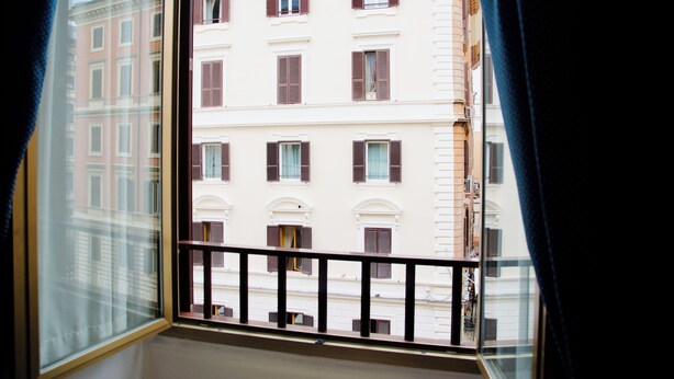 Une vue depuis une fenêtre donnant sur un balcon, avec en contrebas un immeuble doté de nombreuses fenêtres et volets.
