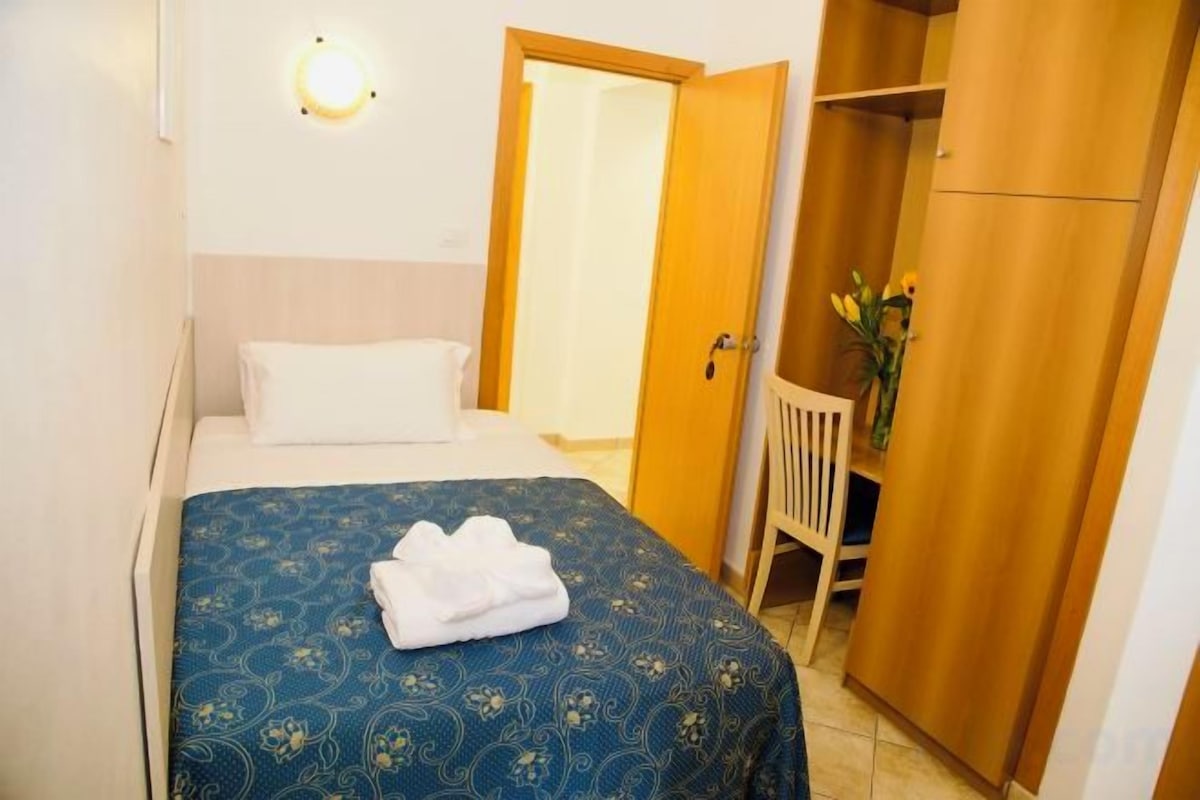 Un dormitorio con cama, mesita de noche, armario y puerta que da a otra habitación.