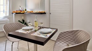 Un coin repas avec une table dressée pour deux personnes, une bouteille de vin et une assiette de fruits disposée sur une étagère au-dessus.