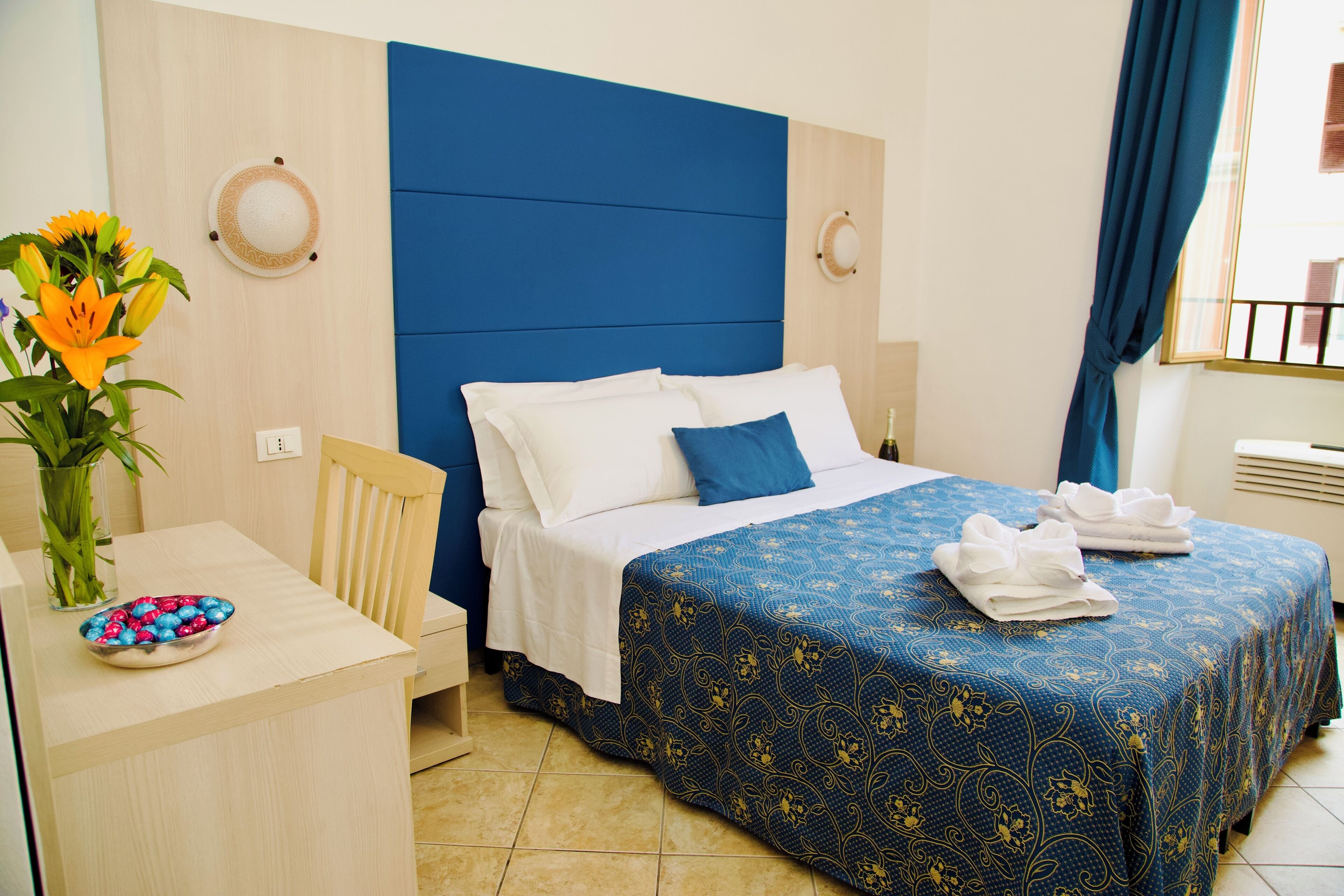 A hotel room with a bed, bedside table, and a vase with flowers.