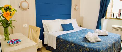 A hotel room with a bed, bedside table, and a vase with flowers.