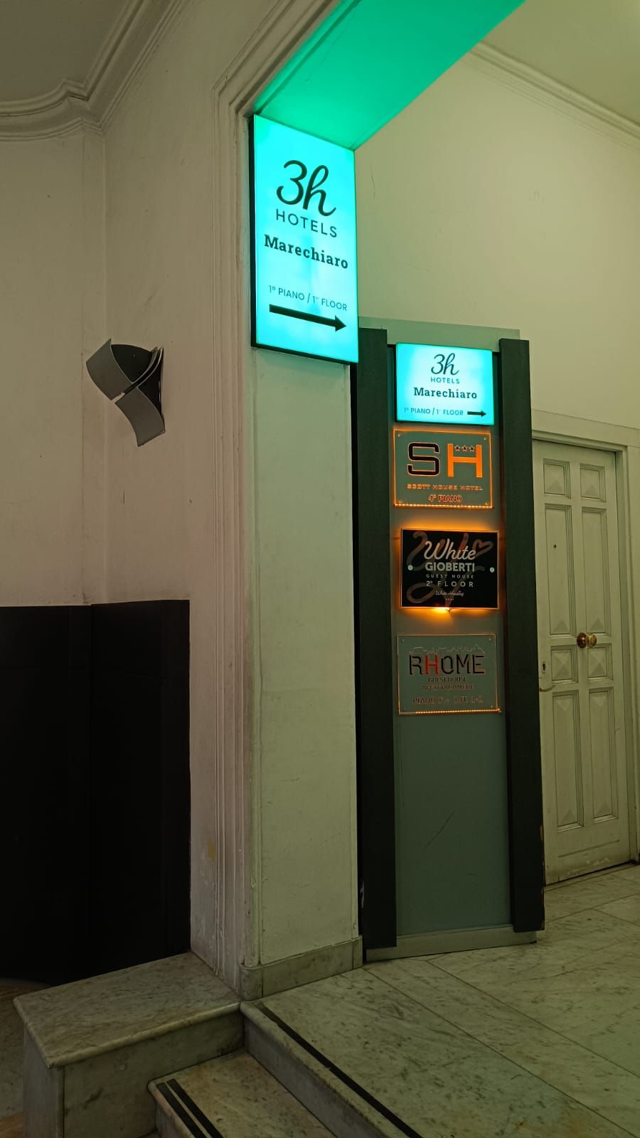 A hotel entrance with a sign for 3h Hotels Marechiaro, a piano on the 1st floor, and a guest house on the 2nd floor.