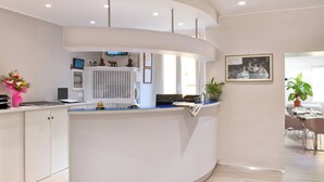 Un espace d’accueil avec un bureau incurvé, un radiateur blanc, un téléviseur et une photographie encadrée accrochée au mur.