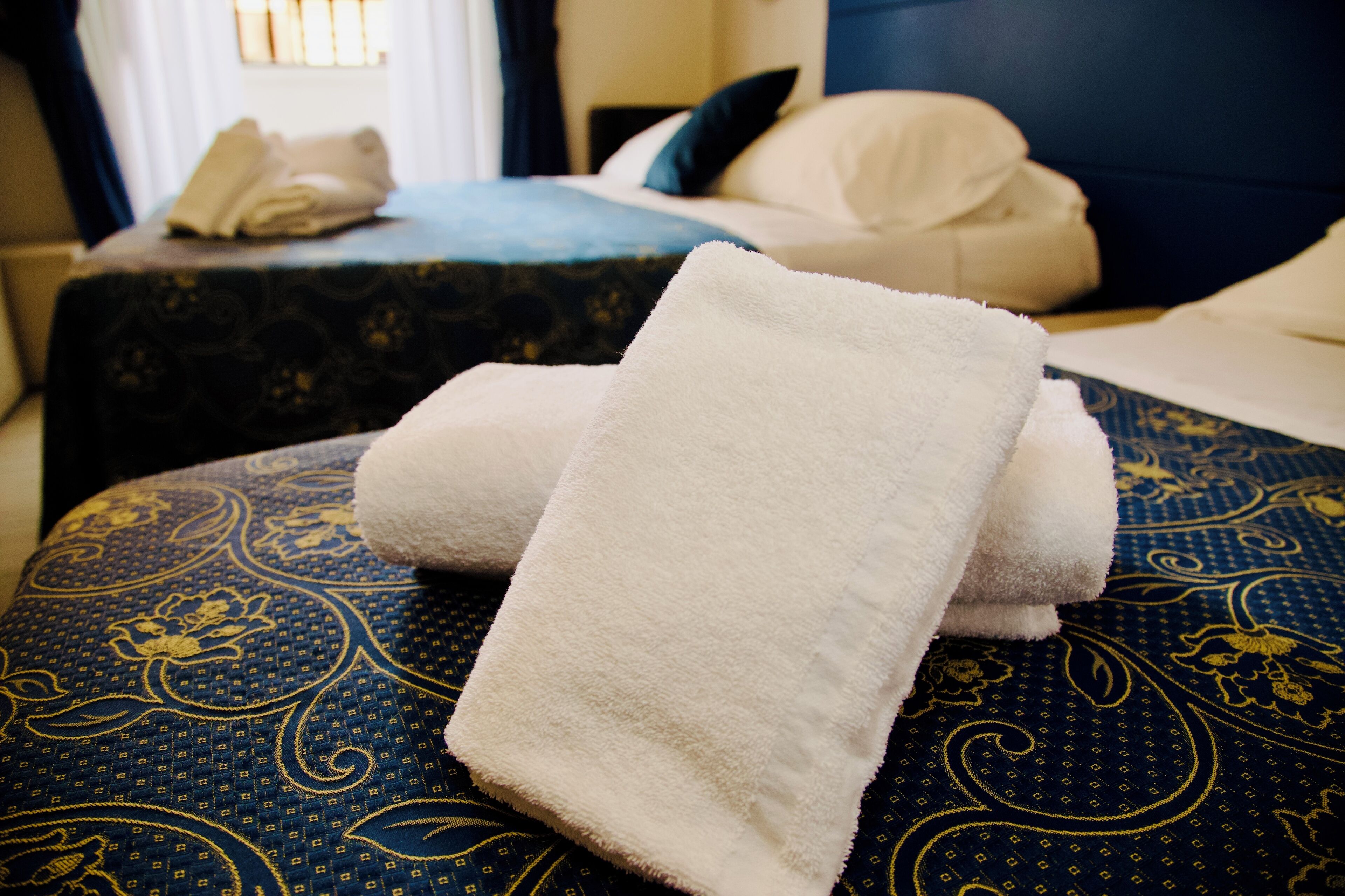 Habitación de hotel con una cama bien hecha, un edredón azul estampado y una toalla blanca sobre la cama.