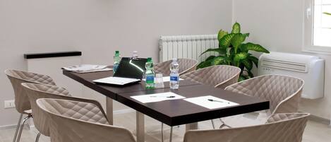 A modern conference room with a large table, six chairs, a flat-screen TV, a radiator, and a potted plant.