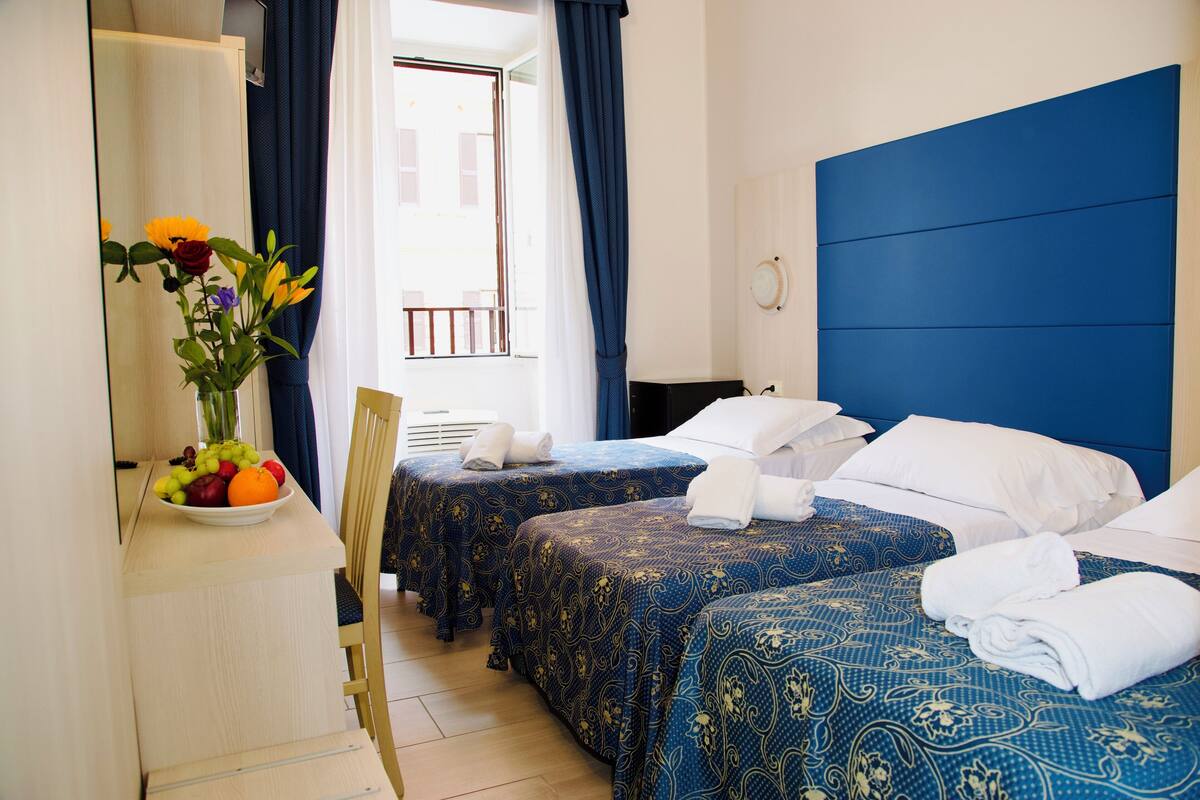 A hotel room with two beds, a desk with a vase of flowers, and a view of the outside balcony.