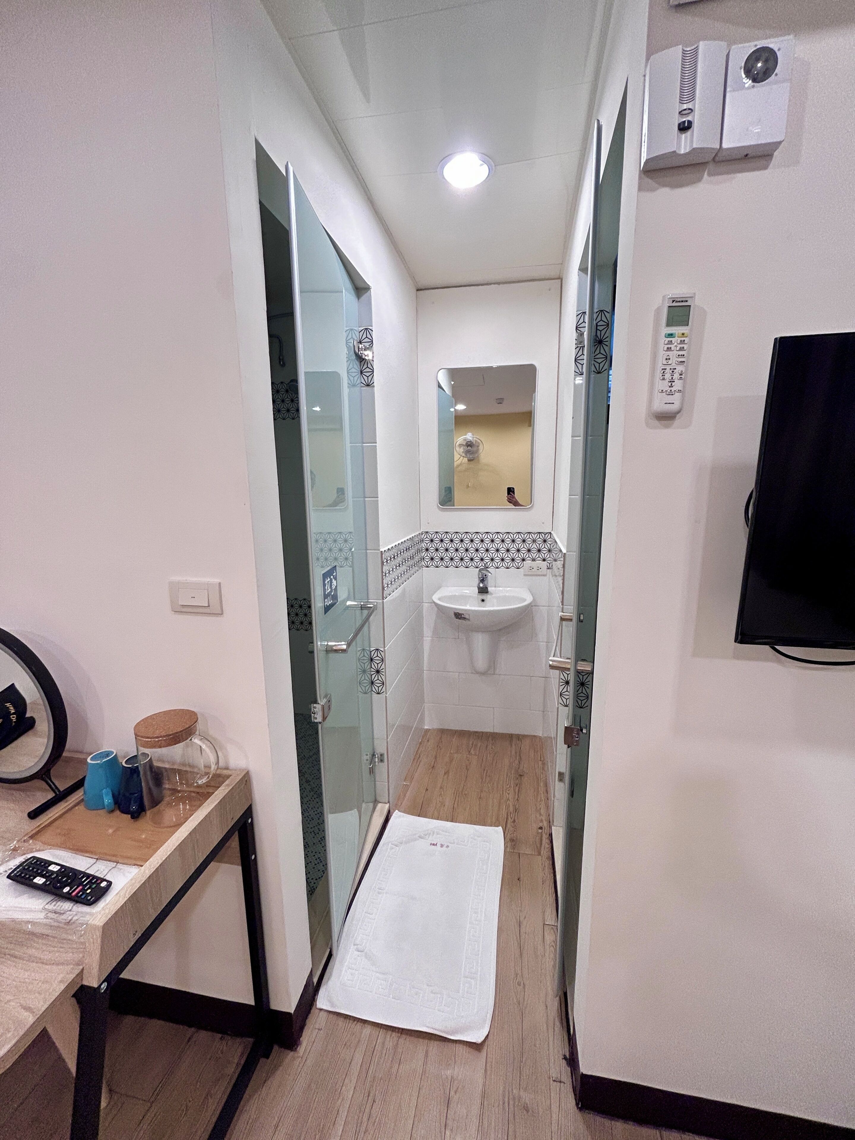 A narrow hallway leading to a bathroom with a sink, a mirror, and a wall-mounted TV.