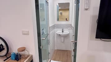 A narrow hallway leading to a bathroom with a sink, a mirror, and a wall-mounted TV.