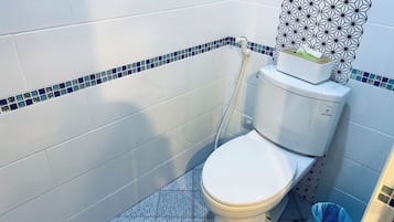 A small bathroom with a toilet, a blue and white tiled floor, and a geometric-patterned shower curtain.