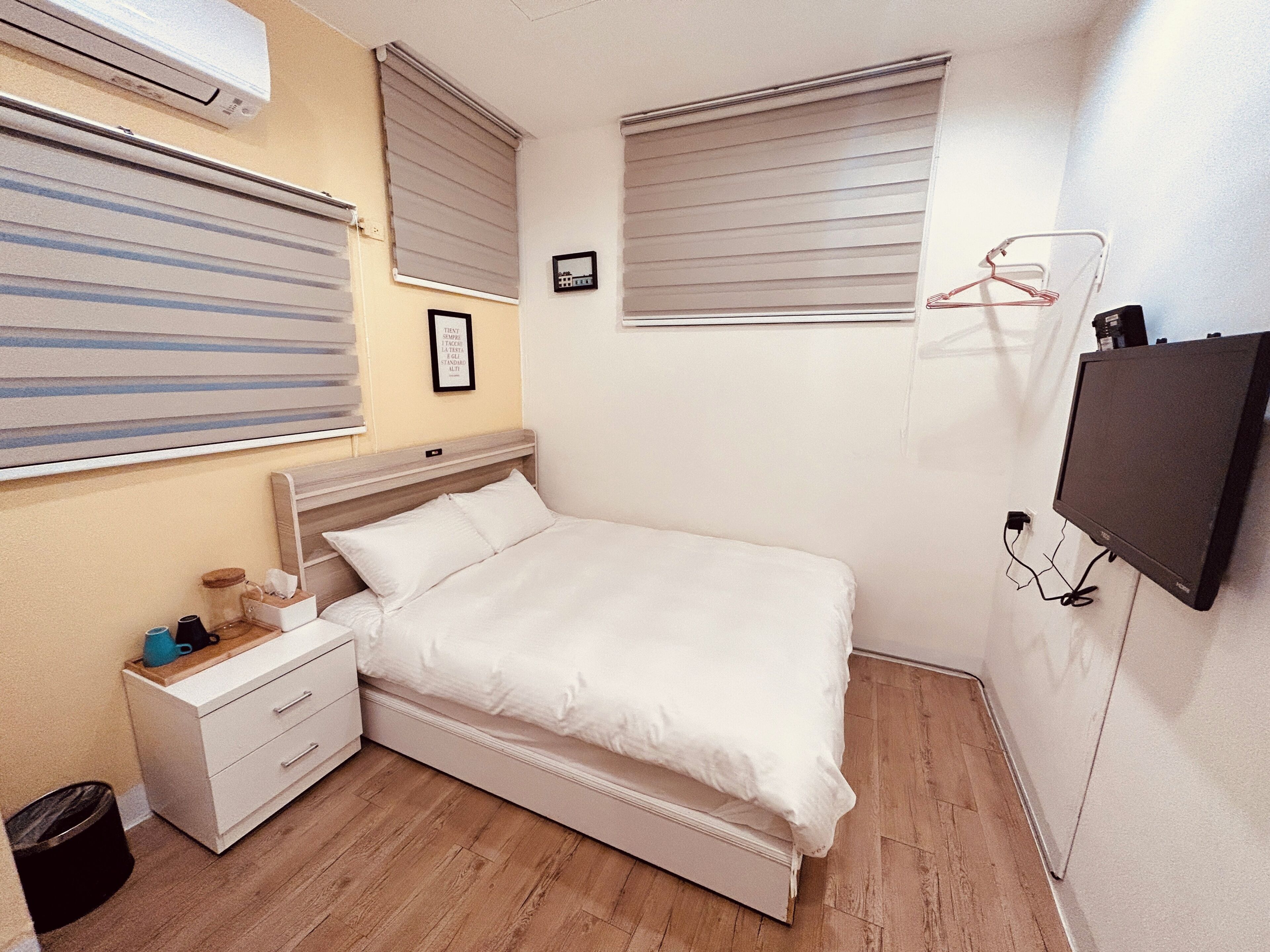 A bedroom with a bed, bedside table, and a TV mounted on the wall.