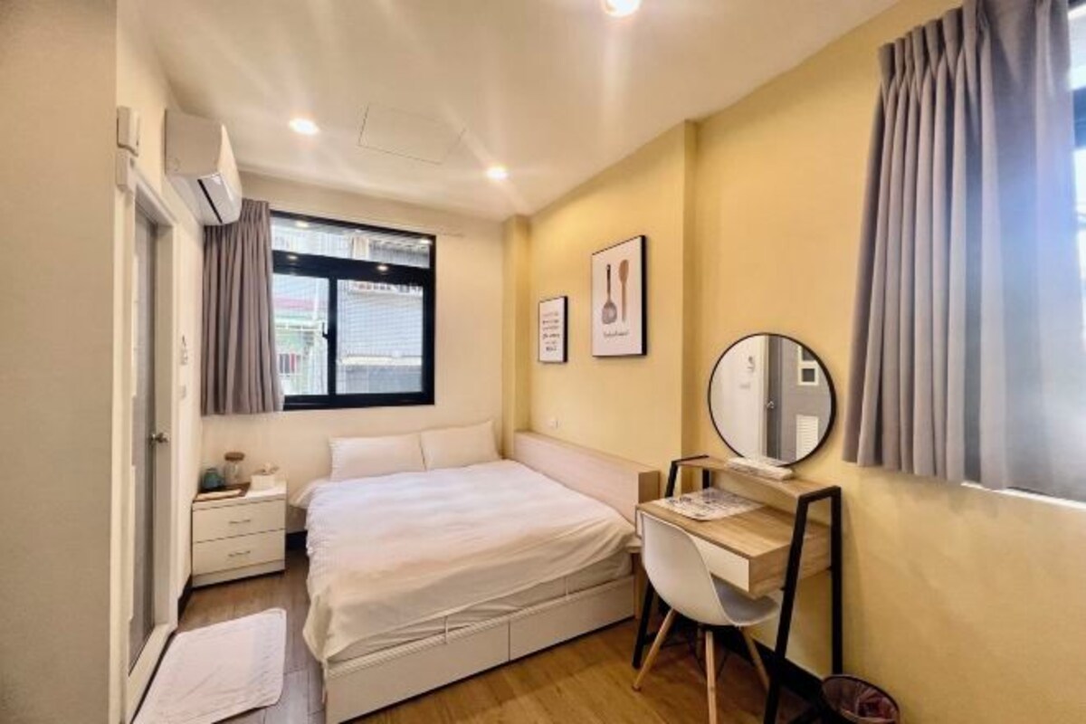 A bedroom with a bed, bedside table, desk, chair, and a mirror.