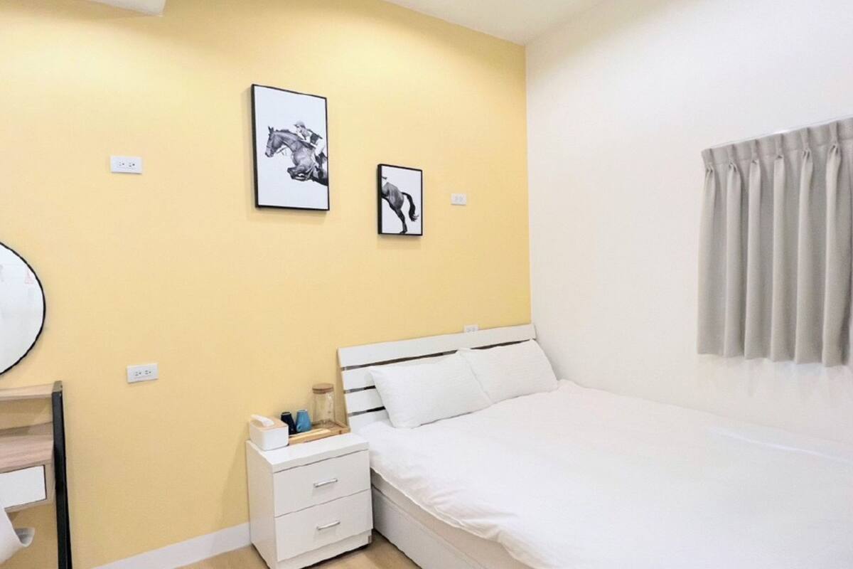 Quarto com cama, mesa de cabeceira e duas molduras na parede.