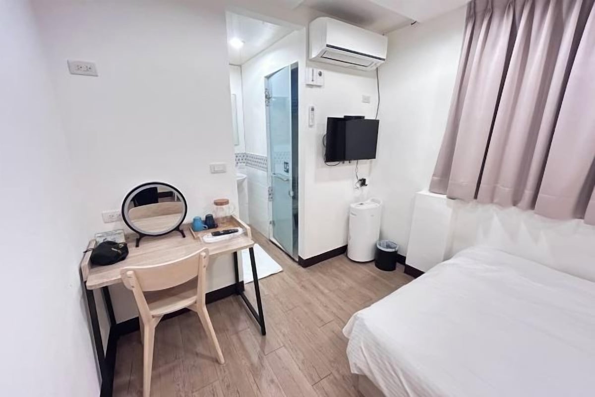 Una camera d'albergo con un letto, una scrivania con una sedia, uno specchio, una televisione e una finestra con tende.