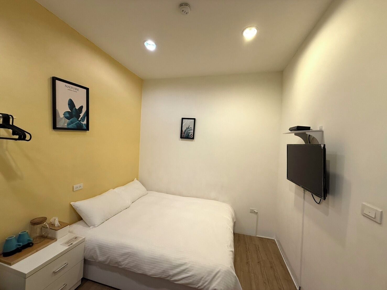 Une chambre d’hôtel comprenant un lit, une table de chevet, un téléviseur fixé au mur et deux appliques murales.