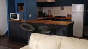 A modern kitchen with a built-in microwave, a gas stove, and a refrigerator. There is a bar stool and a white leather sofa in the foreground. - very nice house, near downtown (Dol-de-Bretagne)
