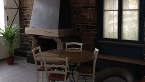 A stone-walled room with a round table and chairs, a large black grill, and a window with decorative glass. - very nice house, near downtown (Dol-de-Bretagne)