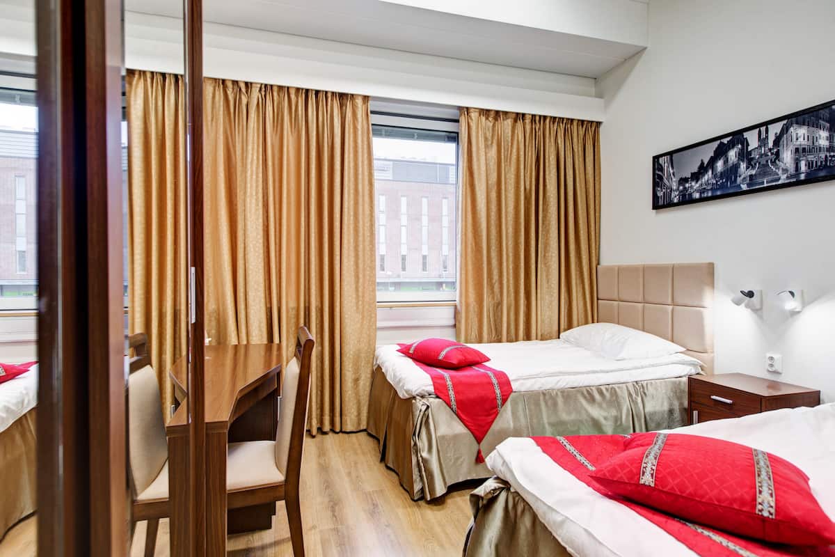 Habitación de hotel con dos camas, un escritorio de madera, una silla y una ventana con cortinas.