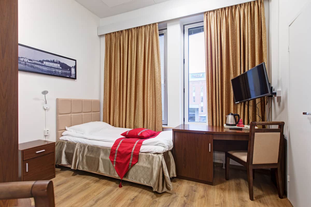 Una habitación de hotel con cama, escritorio, silla, televisor y ventana con cortinas.